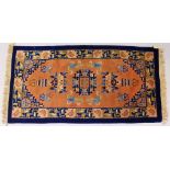 A CHINESE RUG, with blue border, terracotta ground and motifs in blue. 5ft x 2ft 4ins.