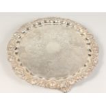 AN ENGRAVED CIRCULAR SALVER, with shell cast border, on scroll feet. 16ins diameter.