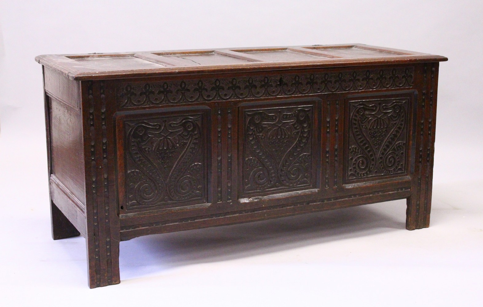 A 17TH CENTURY OAK COFFER, with a four panelled top, over a carved frieze and three carved panels,