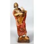 A 17TH-18TH CENTURY CARVED WOOD AND PAINTED PRIEST, holding a lamb on an open book. 24ins high.