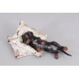 A SMALL COLD PAINTED DOG ON A PILLOW. 3.3ins long.