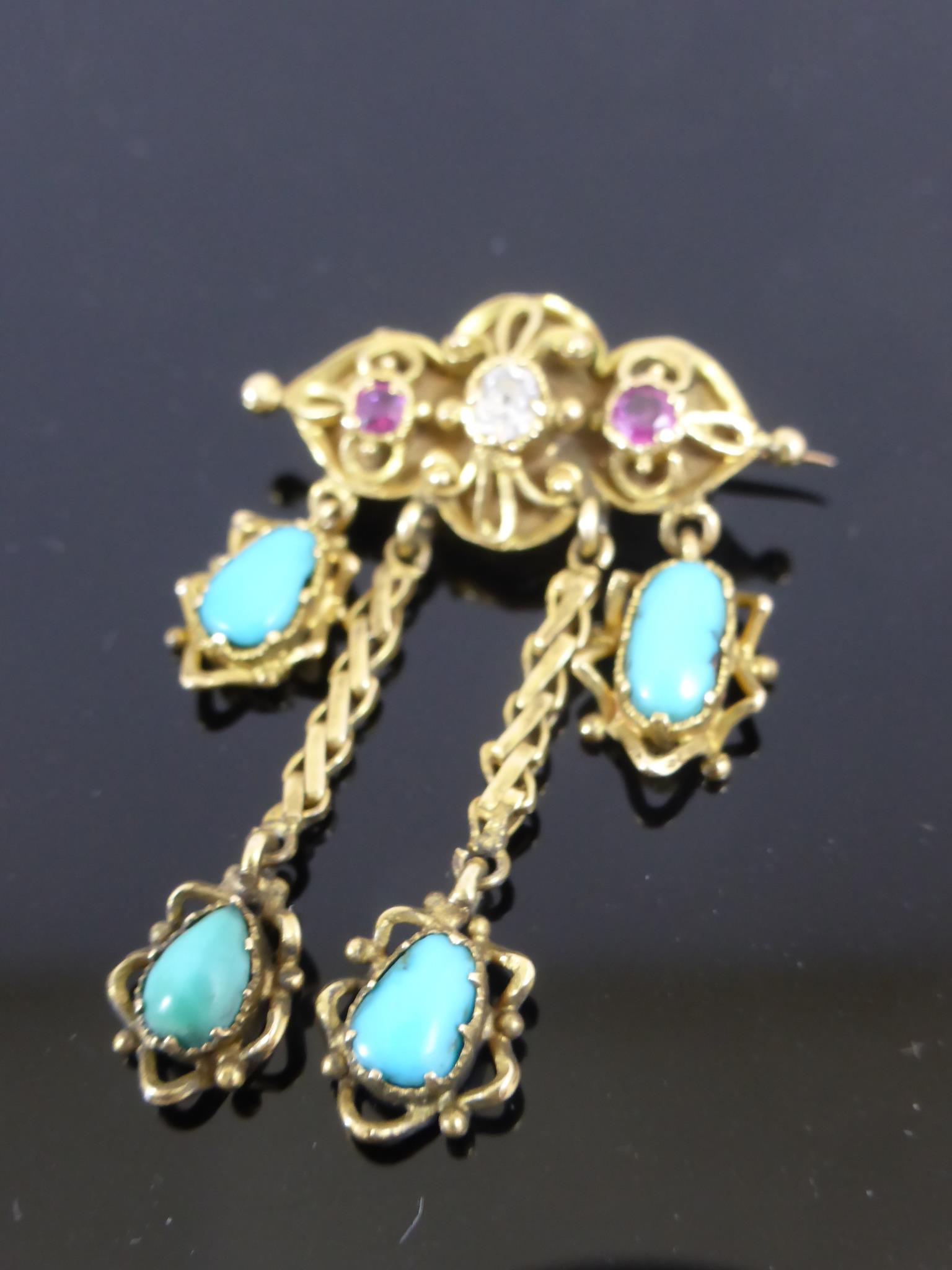 GOLD BROOCH SET WITH A DIAMOND FLANKED BY 2 RUBIES AND HAVING 4 SUSPENDED CABOCHON TURQUOISE