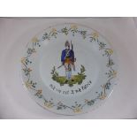 FRENCH FAIENCE PLATE DEPICTING AN 18TH CENTURY INFANTRY MAN, INSCRIBED 'ME VIE EST A MA PATRIE',