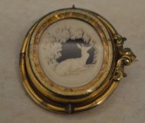 An ornate Victorian Pinchbeck swivel cameo brooch depicting a recumbent deer in a forest,