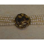A four row pearl necklace with yellow metal clasp with depicting a heron in a naturalistic scene