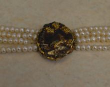 A four row pearl necklace with yellow metal clasp with depicting a heron in a naturalistic scene