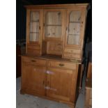 A waxed pine dresser, the upper section fitted three glazed doors over four drawers, two further