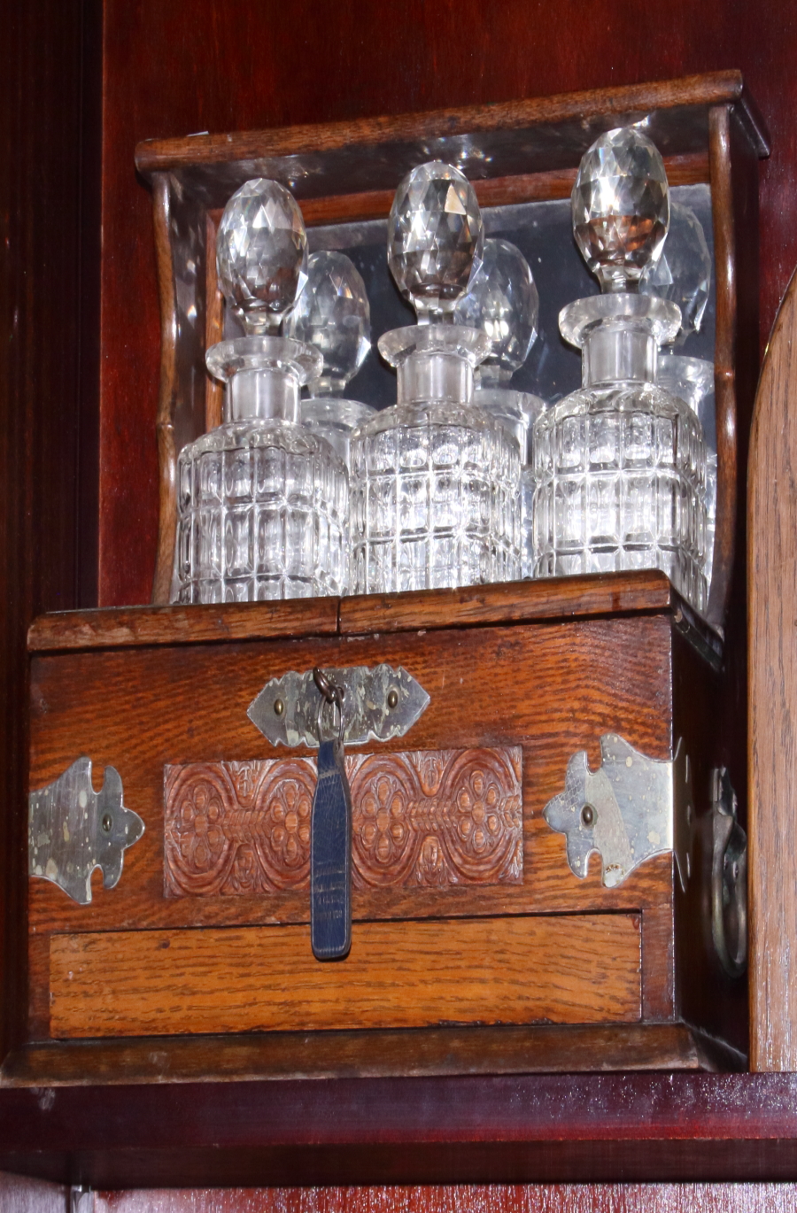 An Edwardian carved oak integrated tantalus/cigar two-handled box with three cut glass decanters, on