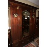 An Arts & Crafts mahogany wardrobe enclosed two shaped glazed panelled doors and central mirror