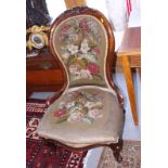 A Victorian carved walnut showframe low seat nursing chair with needlepoint seat and back, on