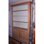 A waxed pine open bookcase, fitted adjustable shelves over cupboard enclosed panelled doors, on