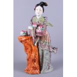 A Chinese porcelain famille rose figure of Kuan Yin holding peaches standing against a tree trunk,