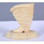 An early 20th century carved ivory egg cup, in the form of a gentleman's boot, on an oval plinth,
