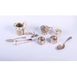 A silver mustard pot, a silver milk jug, two silver napkin rings, two silver spoons, a pair of