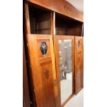 An Arts & Crafts design three door wardrobe, fitted centre mirror door flanked by two doors inlaid