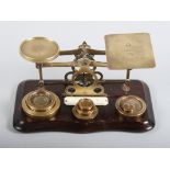 A set of brass postal scales with seven weights, on mahogany base