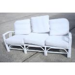 A white painted rattan three-seat settee with loose white cushions