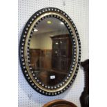 A 19th century oval wall mirror, in black and silvered frame decorated glass beads, 28" x 22" (