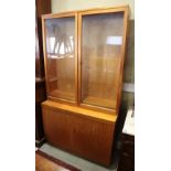 A teak two-stage bookcase, the upper section enclosed glazed doors over base fitted cupboards, 40"