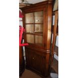 A well reproduced oak corner cupboard enclosed glazed panel door over cupboards, on bracket feet,