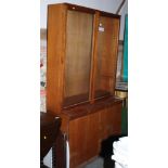 A teak two-stage bookcase, the upper section enclosed glazed doors over base fitted cupboards, 40"