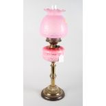 A Victorian oil lamp with pink glass reservoir and shade, on brass pillar
