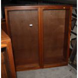 A teak two-stage bookcase, the upper section enclosed glazed doors over base fitted cupboards, 40"