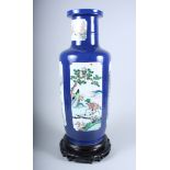 A Chinese porcelain famille rose rouleau vase decorated with panels of country scenes on a blue