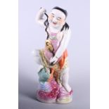 A Chinese porcelain figure of a man adorned with semi-precious objects, his foot raised on the