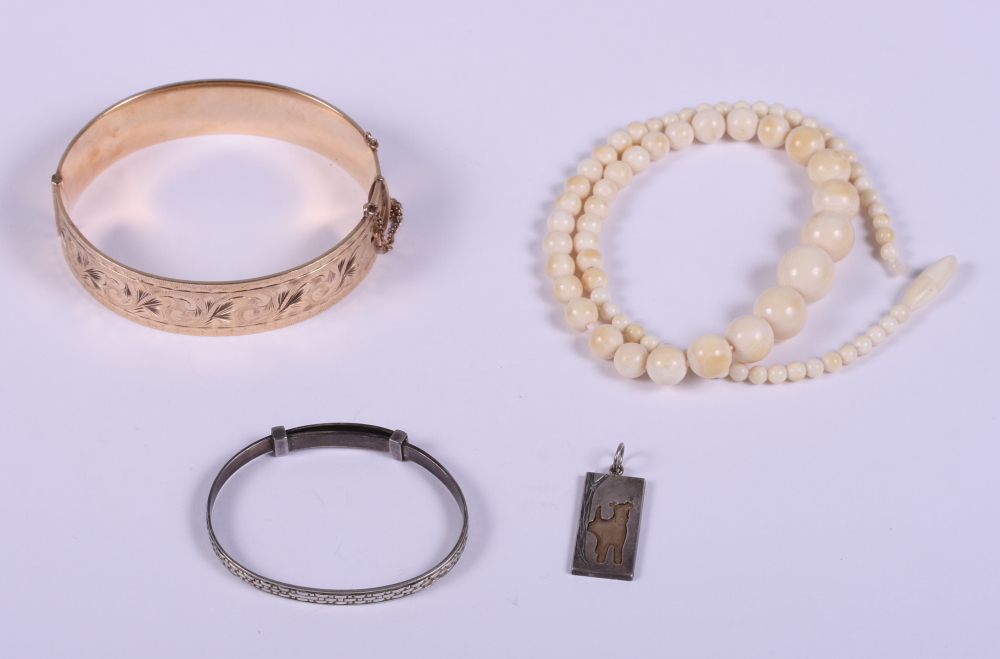 A rolled gold bangle with engraved decoration, a child's silver bangle, an ivory bead necklace and a