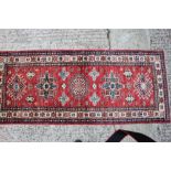 A Kazak style runner with three hooked and two star medallions on a red ground, 78" x 32" approx