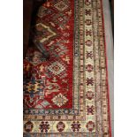 A Kazak design rug with hooked guls on a red ground and mutli-borders in shades of natural, cream,