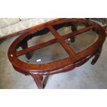 An Oriental hardwood oval low occasional table with sectional smoked glass top, 48" max dia