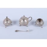 An Indian white metal three-piece cruet set embossed with scroll decoration, on splay supports