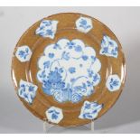 An 18th century Lambeth delft plate with powdered brown ground and reserved panels of chinoiserie