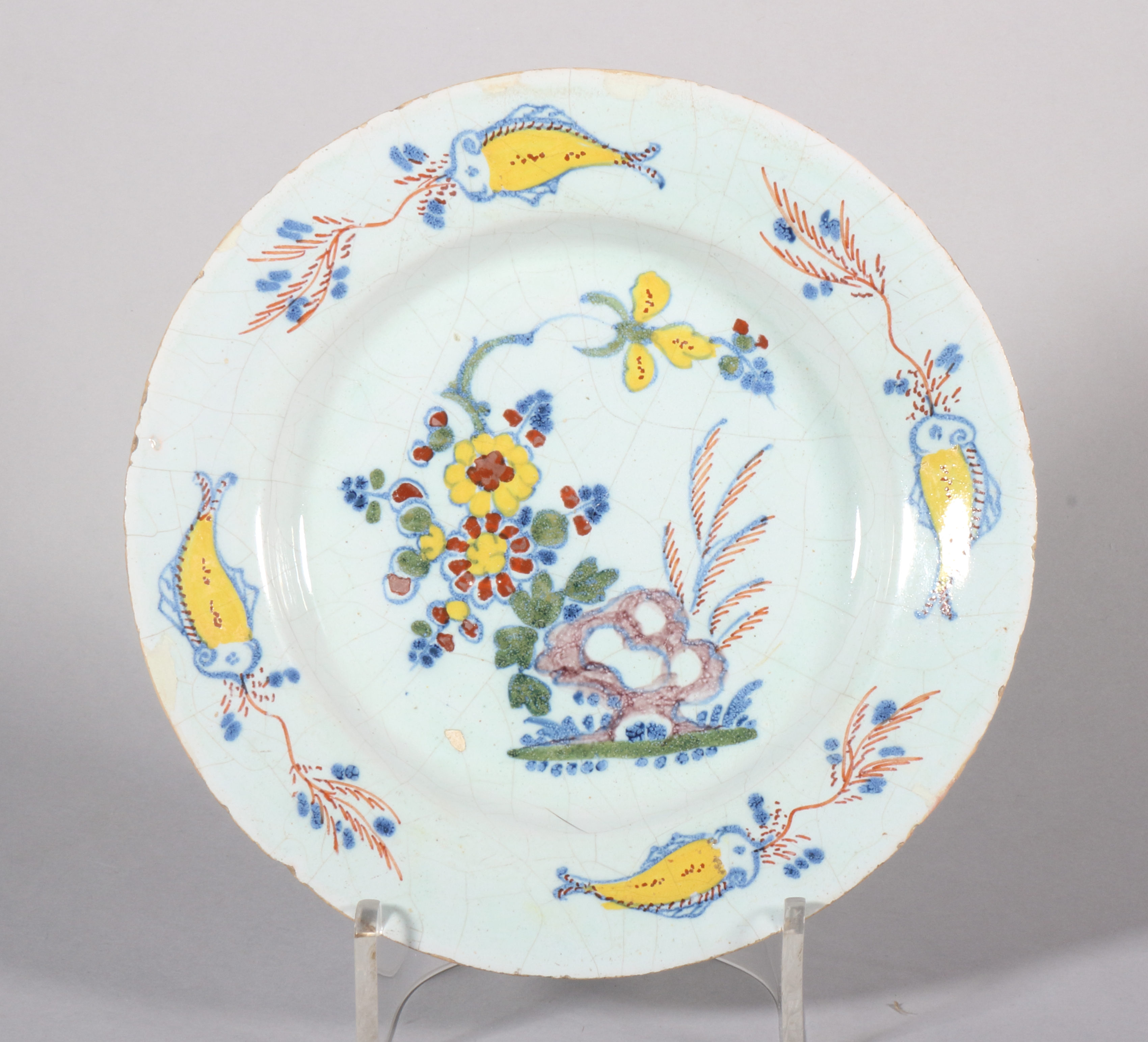 An 18th century English delft plate with polychrome rock and flower decoration and "fish" border,