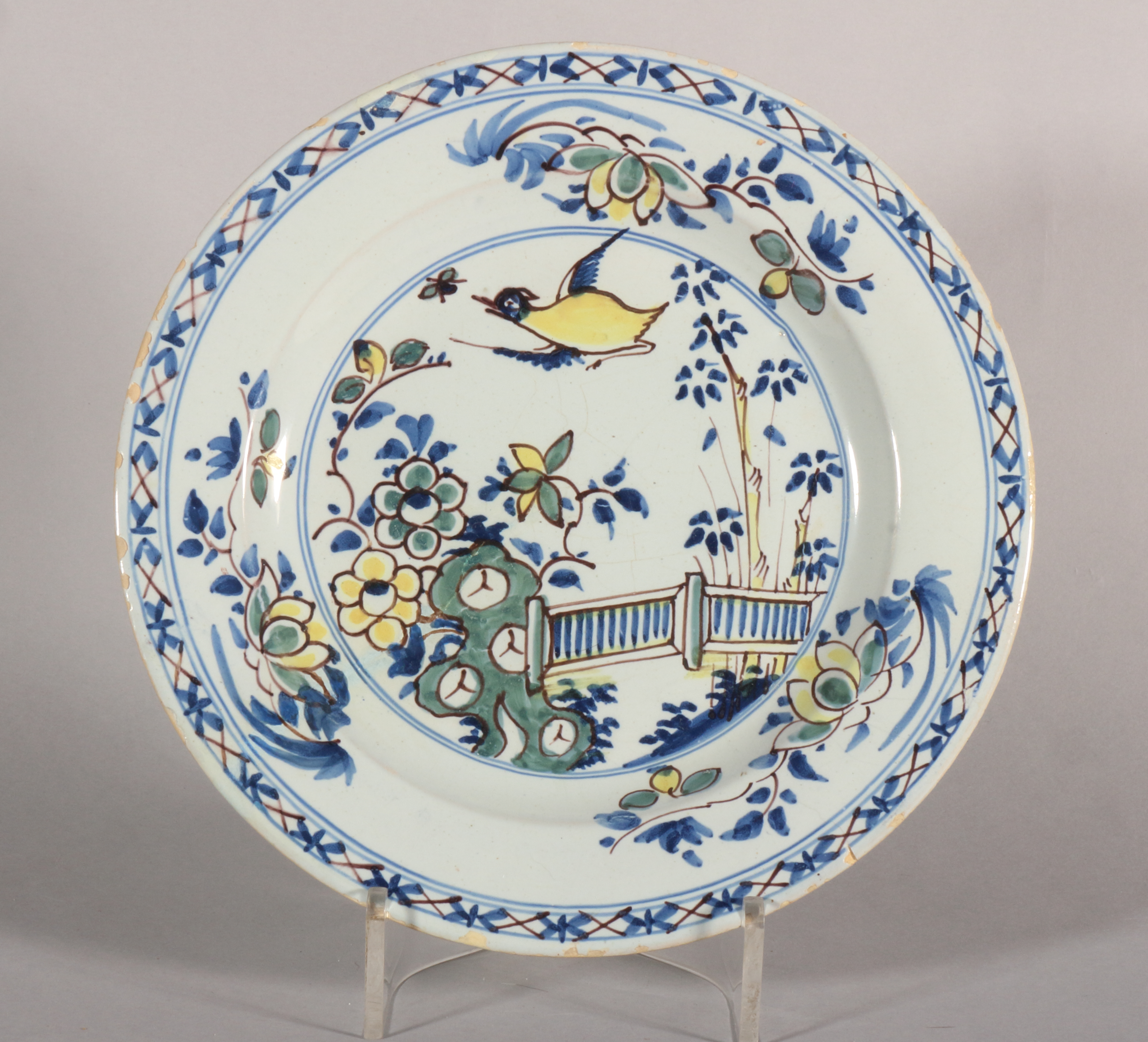 An 18th century London delft polychrome plate with bird, root and fence decoration, 9" dia (