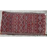 A flat weave rug with all-over geometric design in shades of red, natural, orange, green and pink,