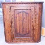 An early 19th century inlaid oak hanging corner cupboard, with single door and applied linen fold