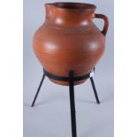 A terracotta water jug, on wrought iron tripod stand