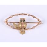 A 9ct yellow and rose gold brooch, in the form of an owl with green enamel eyes sitting on a branch,