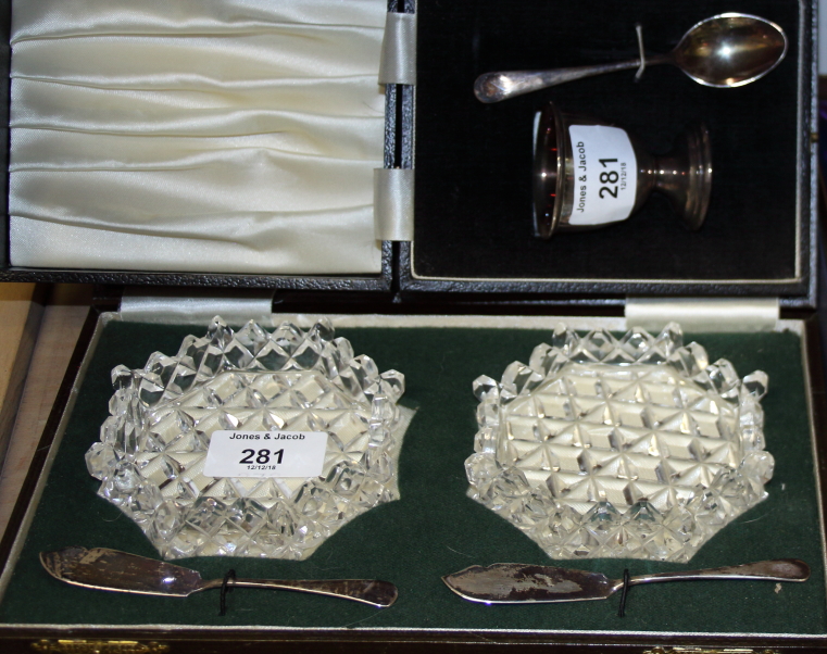 A silver egg cup and spoon set, in case, a pair of cut glass butter dishes with silver butter