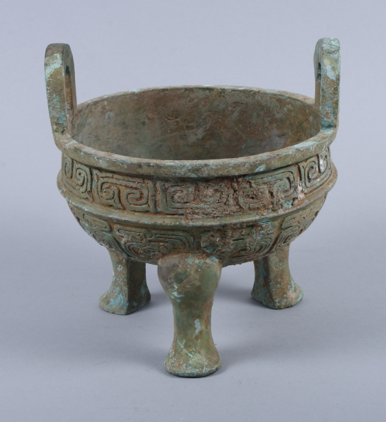 A Chinese bronze Archaic design two-handled foot vessel with relief cast dragon decoration, on three