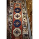 A Kazak design runner with nine guls to the centre, on a salmon ground, 112" x 28" approx