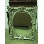 A contemporary oval bevel edged mirror within ornate Continental style silver painted floral frame,