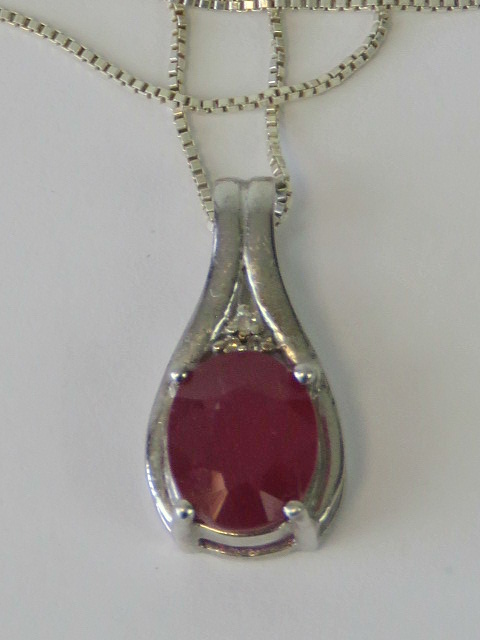 A silver and ruby pendant of teardrop form, large oval cut ruby surmounted by trio of white stones,