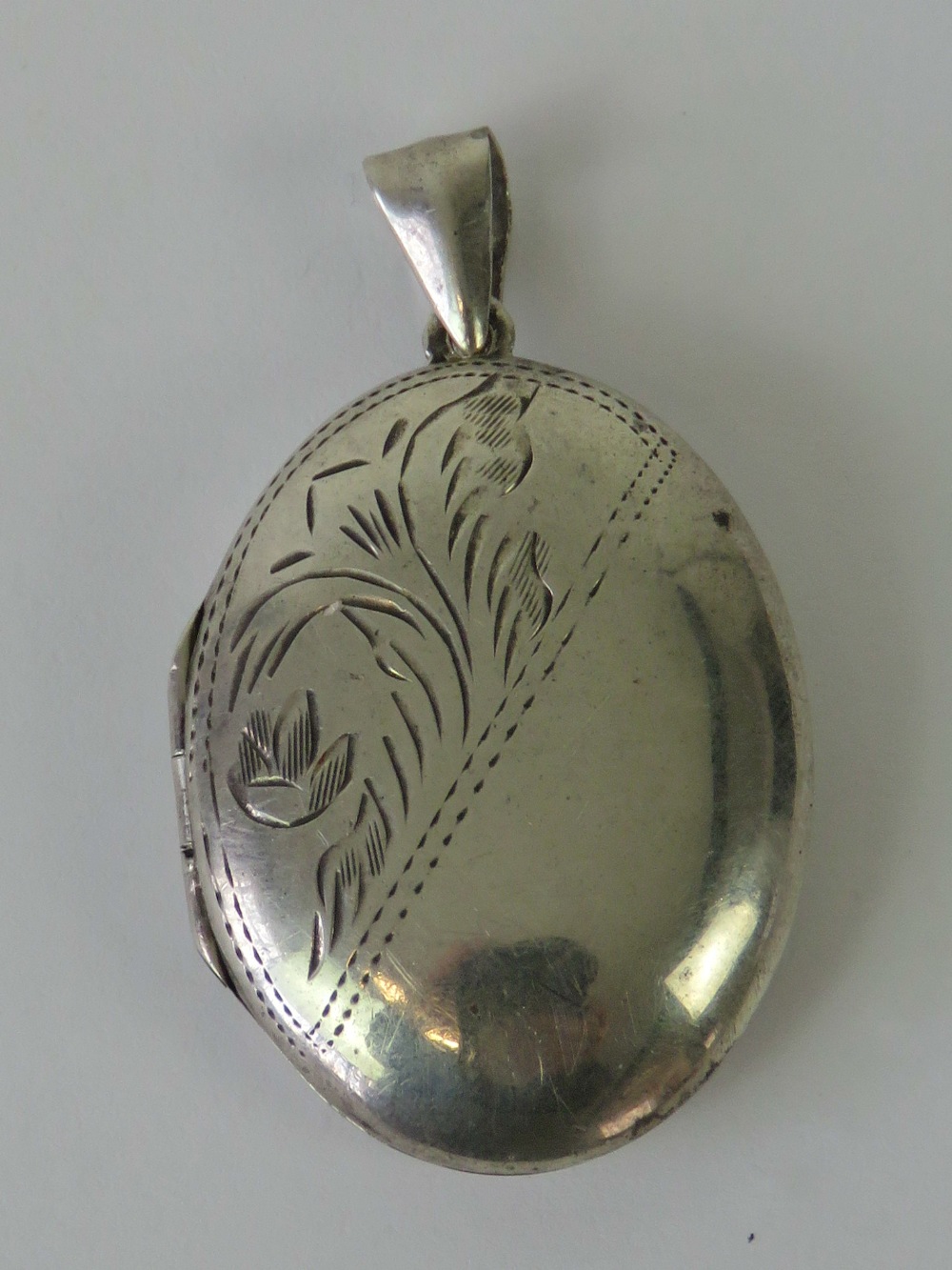 A silver locket of oval form with floral