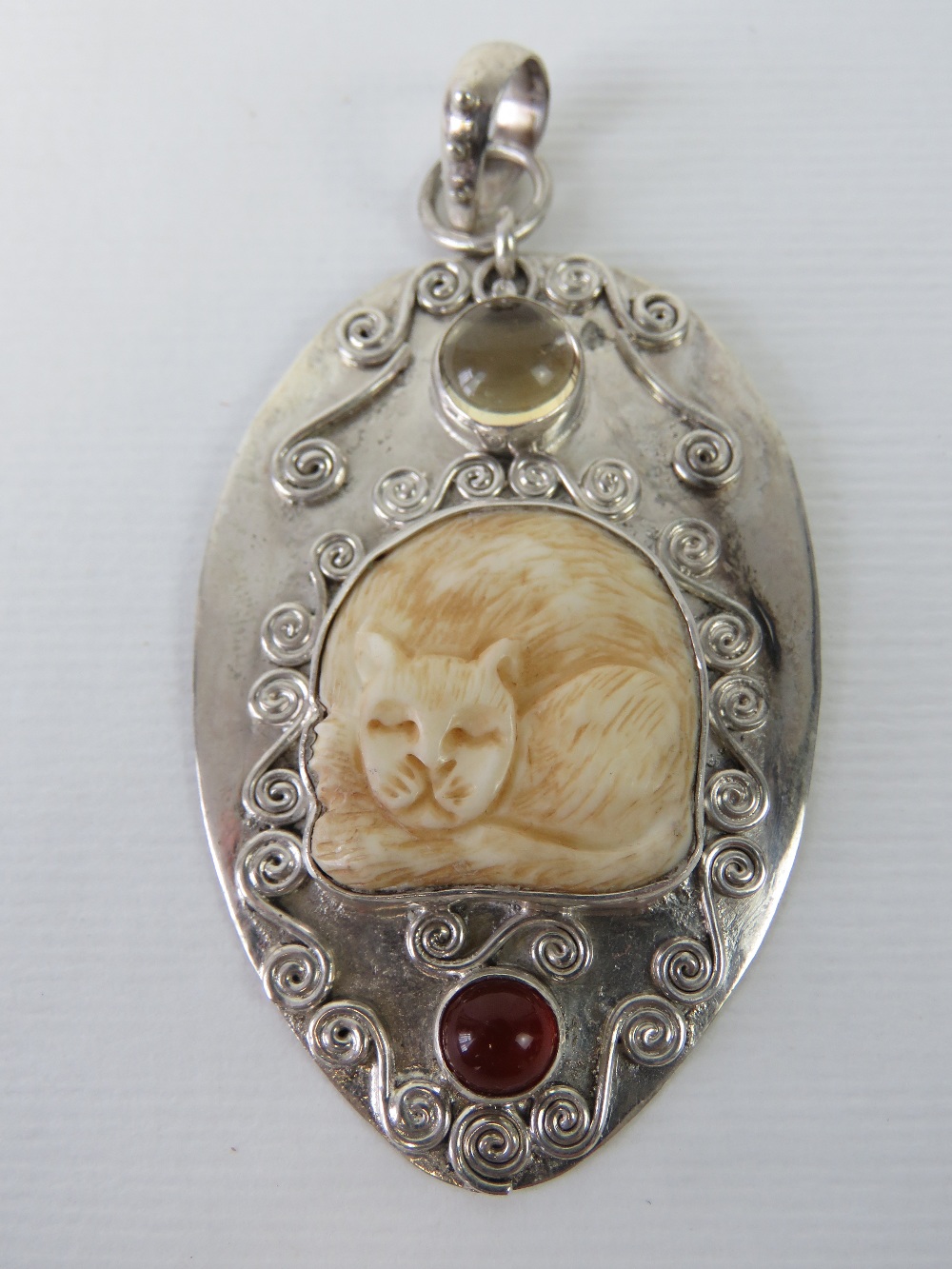 An unusual silver pendant having carved bone cat and two cabachon stones upon,