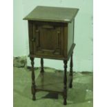 A c1930s oak smokers cabinet on stand, door opening to reveal pipe rack and compartment within,