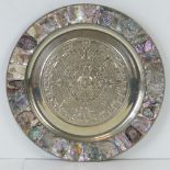 A white metal decorative plate with Azte